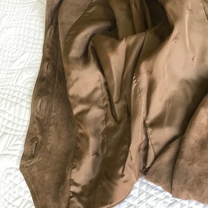 K&ouml;nnte beinhalten: Eine braune Wildlederjacke mit braunem Satin-Futter. Das Futter ist mit dem Wort "Gucci" durchgehend bedruckt.