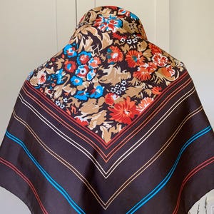 K&ouml;nnte beinhalten: Ein quadratischer Schal mit braunem Hintergrund und einem Blumenmuster in Rot, Blau und Beige. Der Schal hat einen gestreiften Rand mit roten, wei&szlig;en und blauen Linien. Der Schal ist aus seidigem Material.