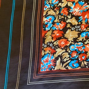 K&ouml;nnte beinhalten: Ein dunkelbrauner Seidenschal mit floralem Muster und gestreiftem Rand. Das florale Design zeigt orange, blaue und wei&szlig;e Blumen auf einem braunen und beigen Hintergrund. Der Rand hat orange, wei&szlig;e und blaue Streifen.