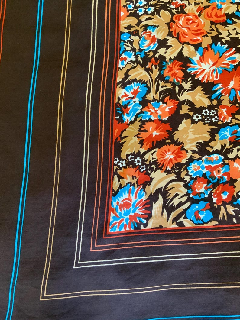 K&ouml;nnte beinhalten: Ein dunkelbrauner Seidenschal mit floralem Muster und gestreiftem Rand. Das florale Design zeigt orange, blaue und wei&szlig;e Blumen auf einem braunen und beigen Hintergrund. Der Rand hat orange, wei&szlig;e und blaue Streifen.