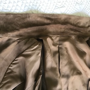 K&ouml;nnte beinhalten: Eine braune Wildlederjacke mit braunem Satin-Futter. Das Futter hat ein sich wiederholendes Muster des Markenlogos.