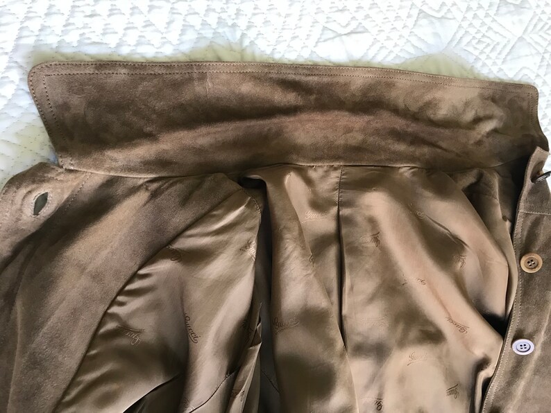 K&ouml;nnte beinhalten: Eine braune Wildlederjacke mit braunem Satin-Futter. Das Futter hat ein sich wiederholendes Muster des Markenlogos.