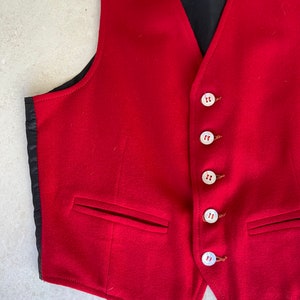 K&ouml;nnte beinhalten: Eine rote Wollweste mit sechs wei&szlig;en Kn&ouml;pfen und zwei Taschen. Die Weste hat ein schwarzes Futter.