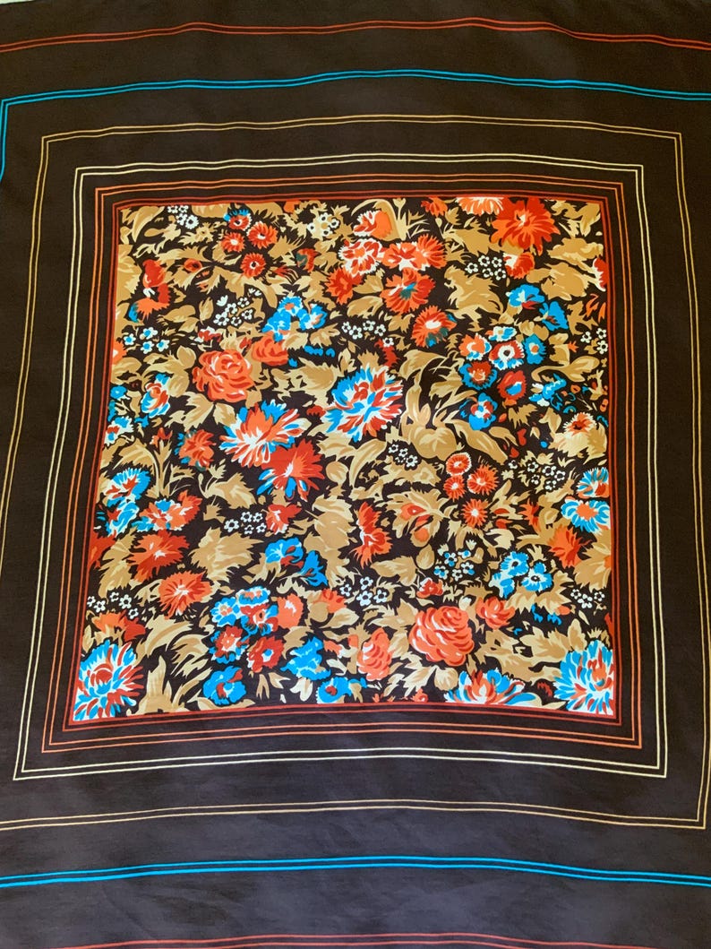 K&ouml;nnte beinhalten: Ein quadratisches Tuch mit einem Blumenmuster in Orange, Blau und Wei&szlig; auf braunem Grund. Der Schal hat einen dunkelbraunen Rand mit orangefarbenen und blauen Streifen.