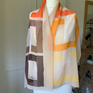 May include: A beige silk scarf with a geometric pattern in shades of orange, yellow, and brown. The scarf has the word "Echo" printed on it.