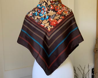 May include: A square scarf with a brown background and a floral pattern in shades of red, blue, and tan. The scarf has brown, red, and blue stripes along the edges. The scarf is displayed on a white mannequin.