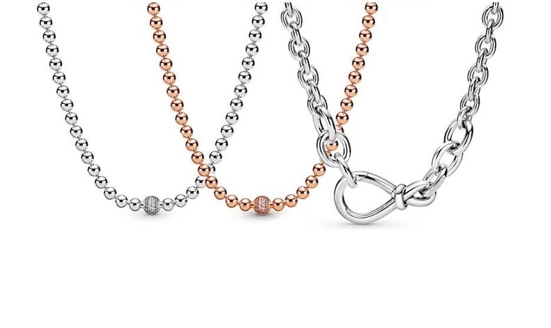 May include: Three silver necklaces with different chain styles. One necklace has a round, pave-set charm. Another necklace has a round, pave-set charm. The third necklace has a knotted, open-loop charm.