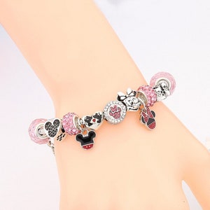 Pu&ograve; includere: Un braccialetto con ciondoli in argento con ciondoli rosa e neri con Mickey Mouse e Minnie Mouse. I ciondoli sono decorati con strass scintillanti.