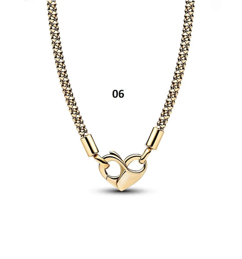 May include: A gold chain necklace with a heart-shaped clasp. The chain is made of small, linked squares. The number 06 is printed on a white background.