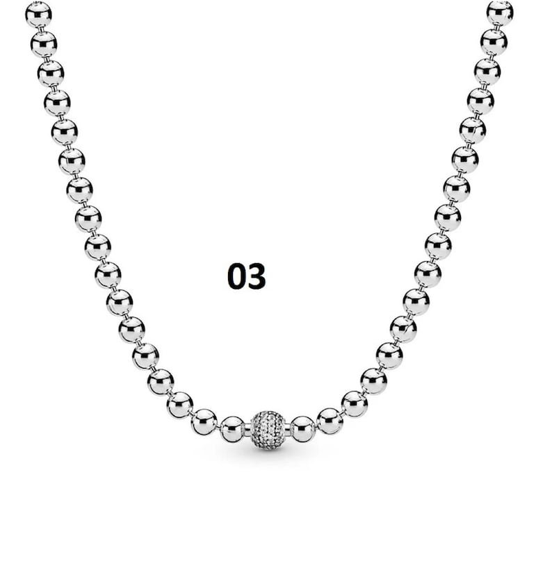 May include: A silver necklace with a round, sparkly charm in the center. The necklace is made of small, round beads.