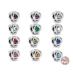 May include: Twelve silver charm beads with different colored gemstones in the center. Each bead is a knot design. The beads are arranged in three rows of four.