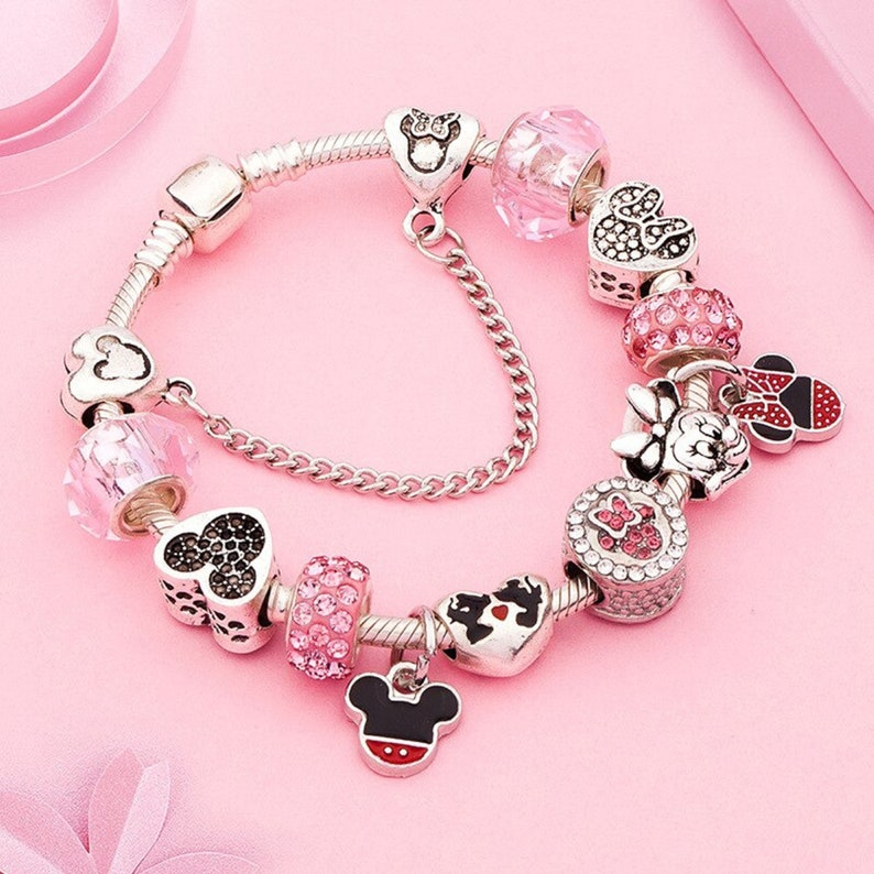 Pu&ograve; includere: Un braccialetto con ciondoli in argento con ciondoli rosa e rossi con Mickey Mouse e Minnie Mouse. I ciondoli sono decorati con strass e fiocchi.