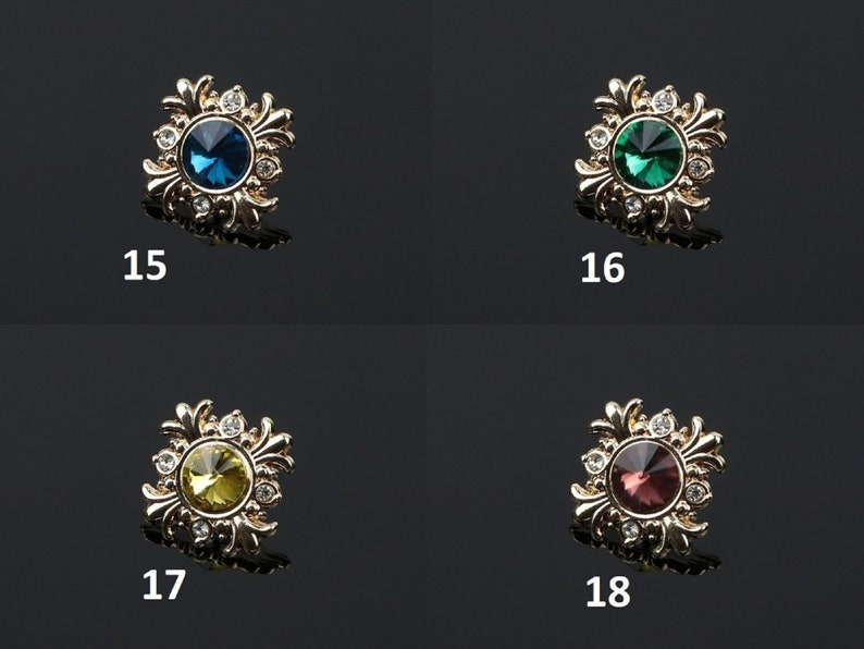 K&ouml;nnte beinhalten: Vier goldfarbene Dekorverzierungen mit einem floralen Design und einem runden, facettierten Edelstein in der Mitte. Die Edelsteine sind blau, gr&uuml;n, gelb und rot.