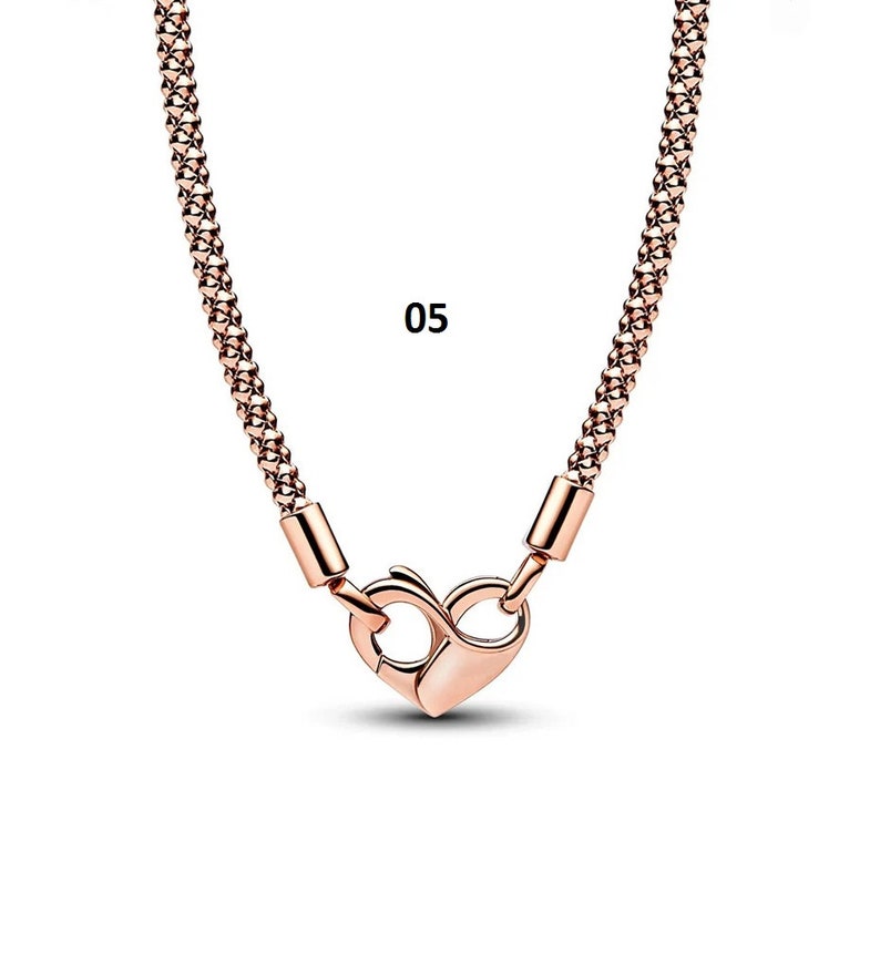 May include: A rose gold chain necklace with a heart-shaped clasp. The chain is made of small, linked squares. The number "05" is visible in the image.