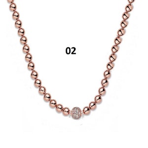 May include: A rose gold necklace with a single larger bead in the center that is encrusted with clear rhinestones. The necklace is made of small round beads.