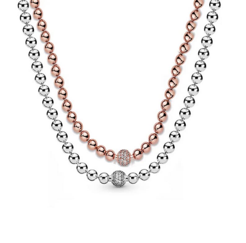 May include: A two-strand necklace with a silver and rose gold bead chain. The necklace has a single, larger bead in the center that is set with clear cubic zirconia stones.