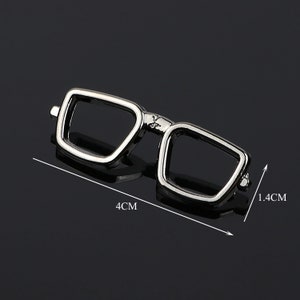 K&ouml;nnte beinhalten: Silberfarbener Anstecknadel aus Metall in Form einer Brille, 4 cm breit und 1,4 cm hoch.