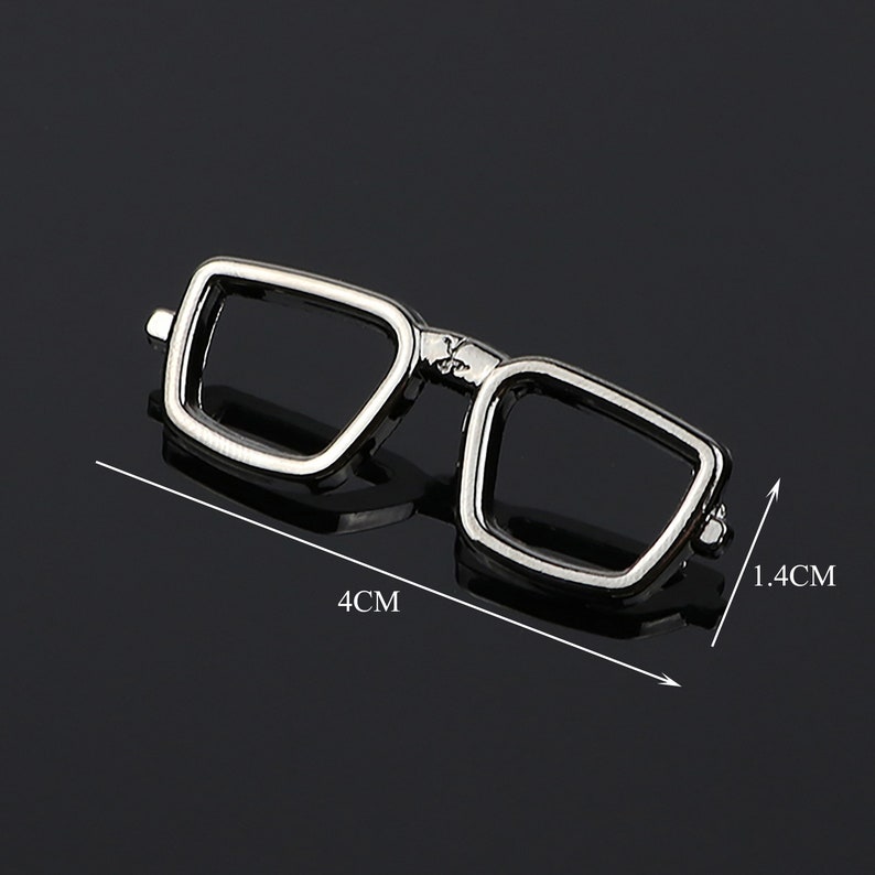 K&ouml;nnte beinhalten: Silberfarbener Anstecknadel aus Metall in Form einer Brille, 4 cm breit und 1,4 cm hoch.
