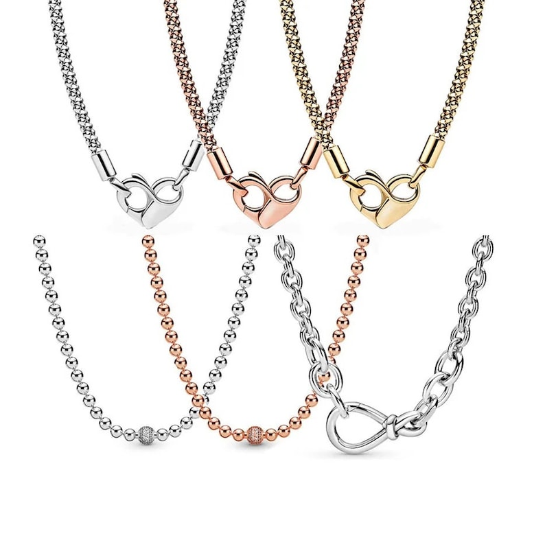 May include: Three silver, gold, and rose gold necklaces with heart-shaped clasps. The necklaces are made of small, linked beads. The silver necklace has a small, round, clear stone charm.