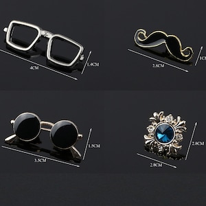 K&ouml;nnte beinhalten: Vier verschiedene Anstecknadeln, jede mit einem anderen Design. Die erste Nadel ist eine silberfarbene Brille, die zweite ist ein goldfarbener Schnurrbart, die dritte ist eine schwarze Sonnenbrille und die vierte ist eine goldfarbene Nadel mit einem blauen Edelstein in der Mitte.