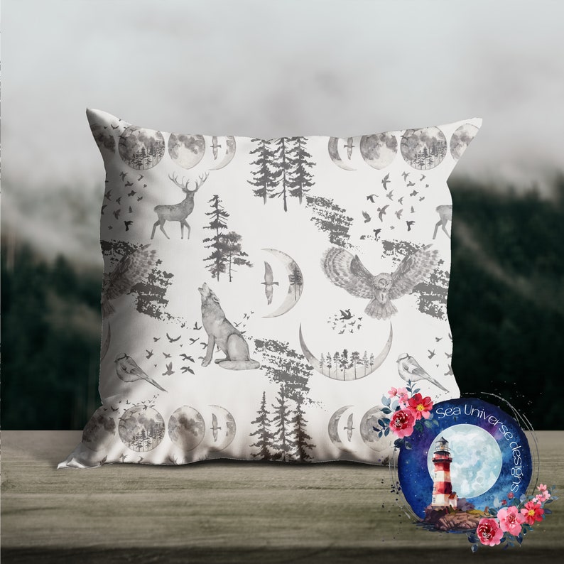 May include: A white throw pillow with a repeating pattern of gray watercolor illustrations of a wolf, deer, owl, trees, and crescent moons. The pillow is on a wooden surface. The text "Sea Universe Designs" is visible in the lower right corner of the image.