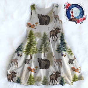 May include: A white sleeveless dress with a woodland animal print. The print features bears, moose, deer, foxes, raccoons, and pine trees. The dress has a gathered skirt.