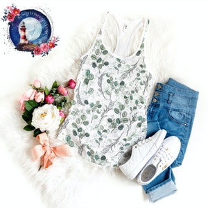 May include: White tank top with a green and white eucalyptus leaf print. The tank top is styled with blue jeans and white trainers.