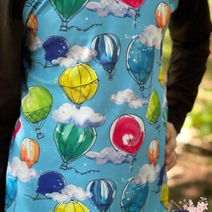 Peut inclure: Un tissu bleu avec un imprimé aquarelle de montgolfières et de nuages. Les ballons sont de différentes couleurs, notamment rouge, vert, jaune et bleu. Le tissu a un design de manche raglan noir et blanc.