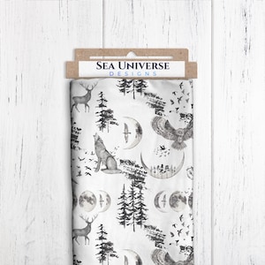 May include: White fabric with a black and gray print of a wolf howling at the moon, a deer, an owl, and trees. The fabric has the text "SEA UNIVERSE DESIGNS" printed on a brown tag.