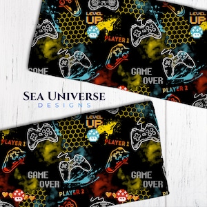 Peut inclure: Tissu noir avec un motif répété de manettes de jeu jaunes et rouges, de nid d'abeille jaune et le texte "LEVEL UP", "GAME OVER", "PLAYER 1" et "PLAYER 2".
