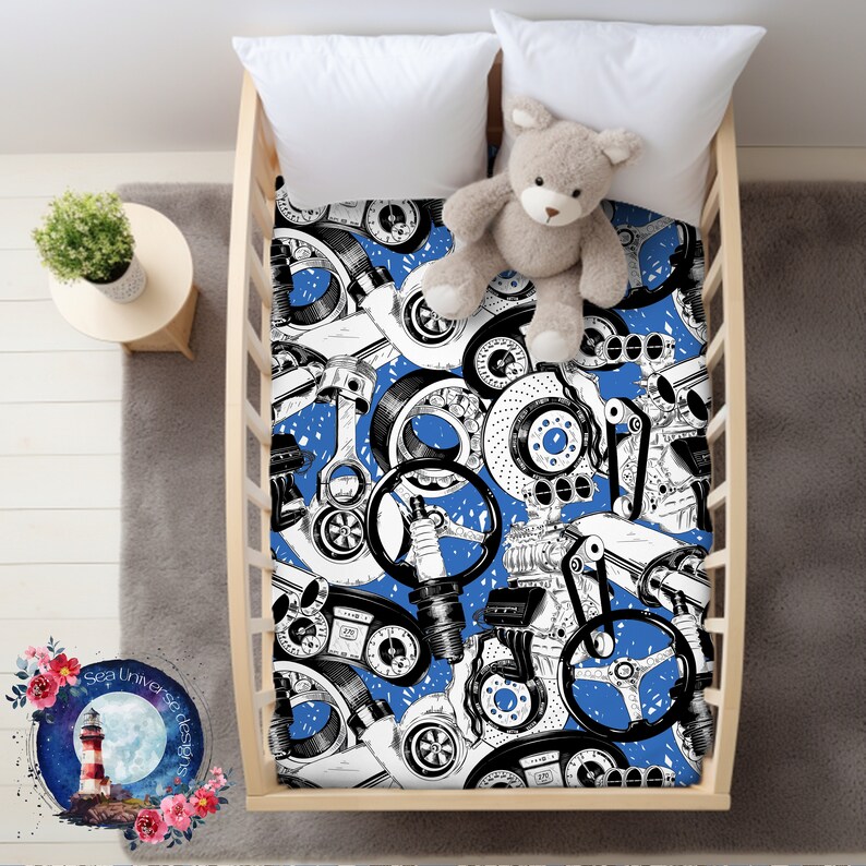 May include: A blue and white crib sheet with a pattern of car parts, including pistons, gears, and wheels. The sheet is in a crib with a teddy bear on top.