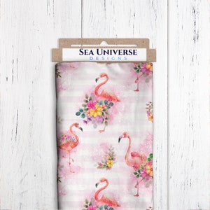 Peut inclure: Tissu rose à rayures blanches avec un motif répété de flamants roses avec des bouquets de fleurs. Le tissu porte l'inscription "SEA UNIVERSE DESIGNS" imprimée sur une étiquette brune.