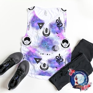 Puede incluir: Un top blanco sin mangas con un estampado de galaxia con lunas, estrellas, cristales, serpientes y manos. El estampado es en tonos de morado, azul y rosa.