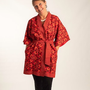 Könnte beinhalten: Eine rote und orangefarbene Kimono-Robe mit floralem Muster und einem schwarzen Gürtel. Die Robe hat eine lange, fließende Silhouette und ist perfekt zum Entspannen zu Hause.