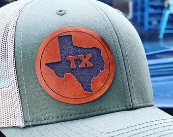 May include: A green and white trucker hat with a brown leather patch featuring the outline of the state of Texas and the letters "TX" in black.