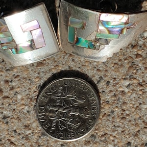 May include: A pair of silver earrings with abalone shell inlay. The earrings are in the shape of a geometric design. The earrings are about the size of a dime.