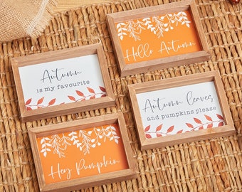May include: Four wooden signs with autumn-themed sayings. The signs have a brown wood frame and an orange background with white and brown leaf designs. The signs read "Hello Autumn", "Autumn is my favourite", "Autumn leaves and pumpkins please", and "Hey Pumpkin".