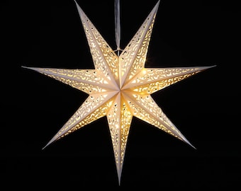 May include: A large, white, eight-pointed star-shaped paper lantern with intricate cut-out designs. The star is illuminated from within, creating a warm, inviting glow. The lantern is suspended from a clear string against a black background. A decorative holiday item.