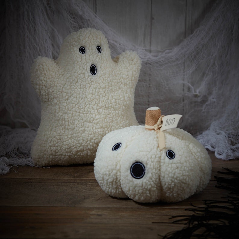May include: Two plush Halloween decorations: a ghost and a pumpkin. The ghost is white with black embroidered eyes and mouth. The pumpkin is also white, with black embroidered eyes and mouth, and a small tag that says "BOO".