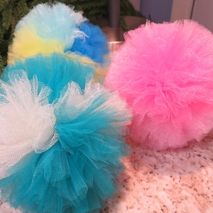 以下が含まれることがあります： ピンク、白、青、黄色の色合いの、カラフルでふわふわのチュールポンポンのコレクション。 ポンポンはまだらの表面に配置され、背景には緑があります。 これらの装飾品は、工芸品やパーティーの装飾に最適です。