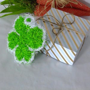 Puede incluir: Una flor de crochet verde y blanca con una textura esponjosa. La flor está encima de una caja de regalo de rayas blancas y doradas.