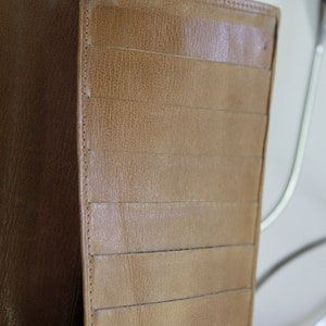 K&ouml;nnte beinhalten: Eine braune Ledergeldb&ouml;rse mit mehreren Kartenf&auml;chern und einem Klappverschluss.