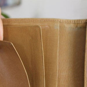 K&ouml;nnte beinhalten: Eine braune Ledergeldb&ouml;rse mit mehreren F&auml;chern und Steckpl&auml;tzen f&uuml;r Karten und Bargeld.