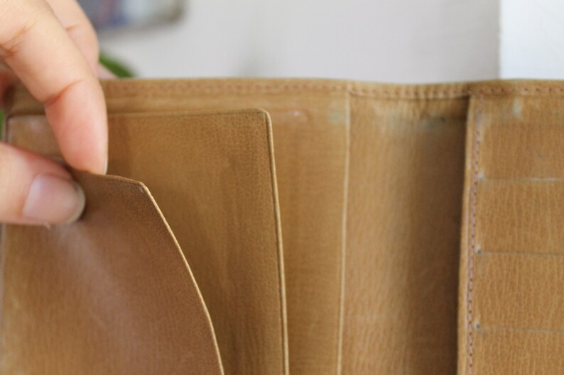 K&ouml;nnte beinhalten: Eine braune Ledergeldb&ouml;rse mit mehreren F&auml;chern und Steckpl&auml;tzen f&uuml;r Karten und Bargeld.