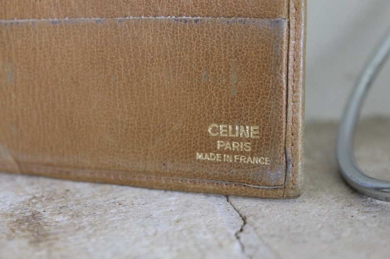 K&ouml;nnte beinhalten: Eine braune Ledergeldb&ouml;rse mit goldener Aufschrift "CELINE PARIS MADE IN FRANCE".