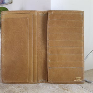 K&ouml;nnte beinhalten: Eine braune Ledergeldb&ouml;rse mit mehreren Kartenf&auml;chern und einem Geldscheinfach. Die Geldb&ouml;rse ist ge&ouml;ffnet und das Innere ist sichtbar. Der Markenname "CELINE PARIS" ist in Gold auf der Innenseite der Geldb&ouml;rse aufgedruckt.