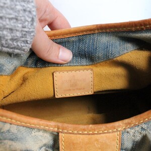 May include: A blue denim handbag with tan leather trim and a mustard yellow interior lining. A rectangular tan leather patch is stitched inside, embossed with the text LOUIS VUITTON PARIS MADE IN FRANCE. The bag features a monogram pattern.