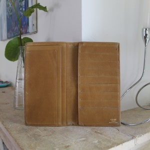 K&ouml;nnte beinhalten: Eine braune Ledergeldb&ouml;rse mit mehreren Kartenf&auml;chern und einem Geldscheinfach. Die Geldb&ouml;rse ist ge&ouml;ffnet und das Innere ist sichtbar. Der Markenname "CELINE PARIS" ist auf der Innenseite der Geldb&ouml;rse aufgedruckt.