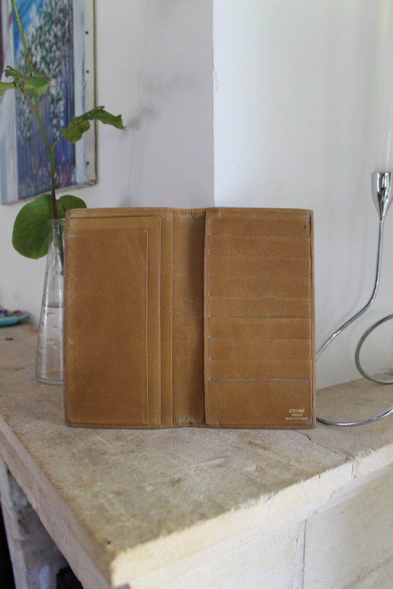 K&ouml;nnte beinhalten: Eine braune Ledergeldb&ouml;rse mit mehreren Kartenf&auml;chern und einem Geldscheinfach. Die Geldb&ouml;rse ist ge&ouml;ffnet und das Innere ist sichtbar. Der Markenname "CELINE PARIS" ist auf der Innenseite der Geldb&ouml;rse aufgedruckt.