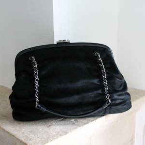 May include: A black, fluffy clutch bag with a silver chain strap.